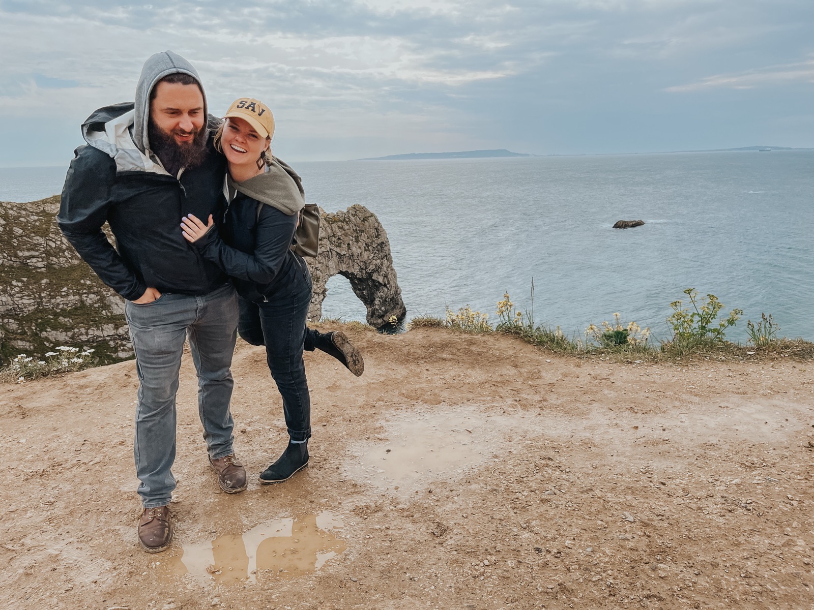 Dani and Kyle laughing on a windy clifftop above the sea