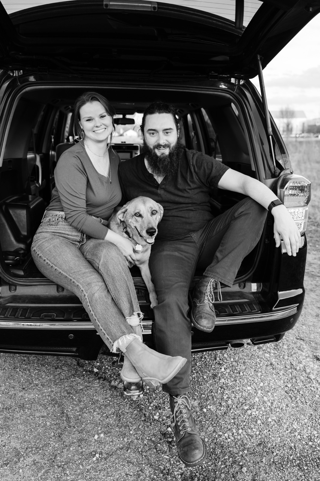Dani and Kyle sitting on the tailgate of their SUV with their dog